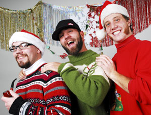 three guys in ugly christmas sweaters with decorations, santa hats, pipe